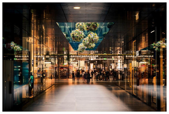 Eine Ladenpassage mit Menschen, glänzenden Glasflächen, Fliesen.