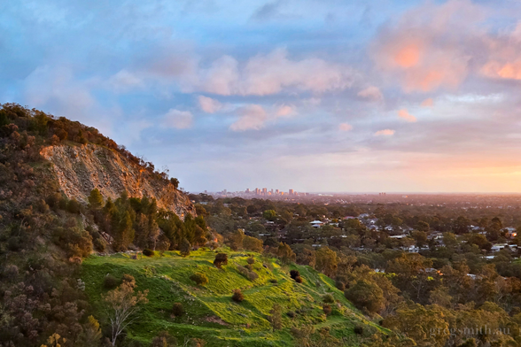 The cliff-face of an abandoned quarry, with the CBD of Adelaide, South Australia in the background, illuminated by the setting sun.