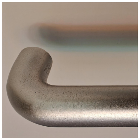 Close up photo of a gray metal door handle that casts slightly offset colour shadows in the off-white door surface behind.