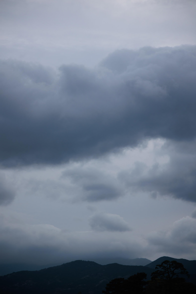 dark, heavy clouds fill most of the sky above a low mountain ridge; the silhouette of a few trees is visible along the ridge in the lower right.