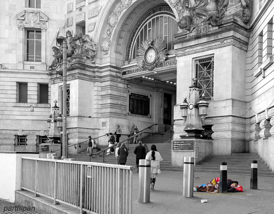 A homeless person is sleeping under a blanket near the entrance to Waterloo Station, while several people are walking up the steps toward the building.

Ein Obdachloser schlaeft unter einer Decke in der Naehe des Eingangs zur Waterloo Station, waehrend mehrere Menschen die Treppe hinauf zum Gebaeude gehen.