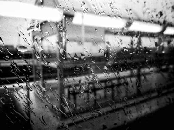 Looking out a rain splattered window towards a train platform in this black and white image.