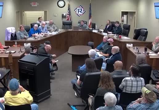 a council meeting where a man with long hair addresses the council and the crowd