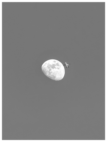This photograph is a black and white one of a gibbous (I think?) moon positioned in the middle against a solid, neutral grey sky. An airplane is visible on the right side of the moon and it looks like it's about to fly directly toward the moon's surface.