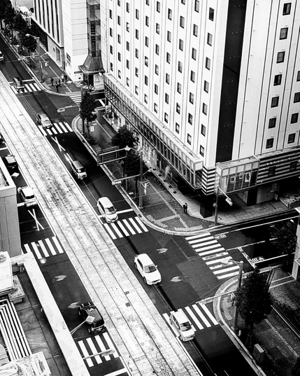 SW Foto,Blick von oben aus einem innerstädtischen Hochhaus auf eine mehrspurige Straße die mehrfach durch Zebrastreifen unterbrochen wird. Das Steifenmotiv findet sich zum Teil auch in der Fassadengestaltung der umgebenden Hochhäuser.