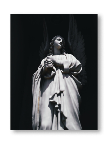 A black and white photo showing a low angle view of a sculpture statue of an angel. Framed in white.