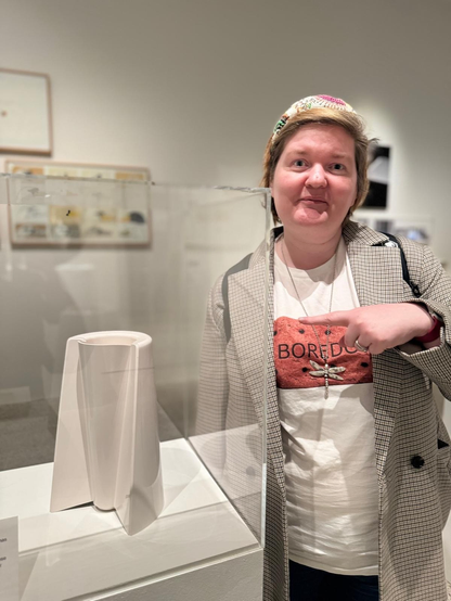 Me, a white woman, pointing at a white enzo mari vase in a museum. 