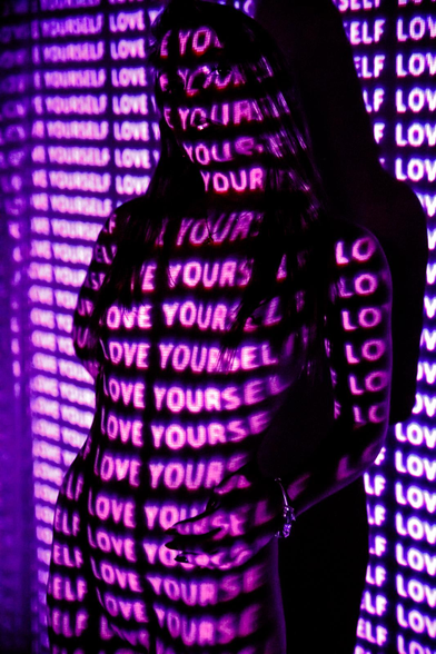 Mujer rubia con letras proyectados sobre el cuerpo.