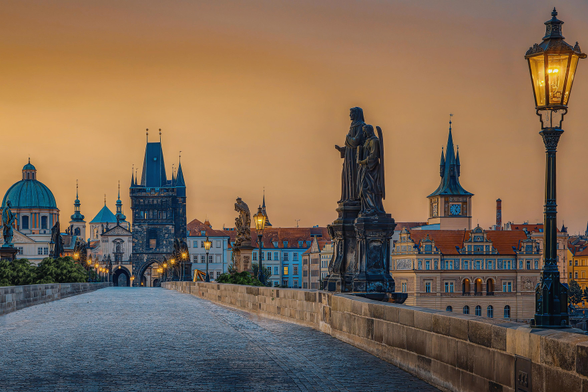 Blick auf die Prager Karlsbrücke und die Altstadt im goldenen Licht der aufgehenden Sonne.