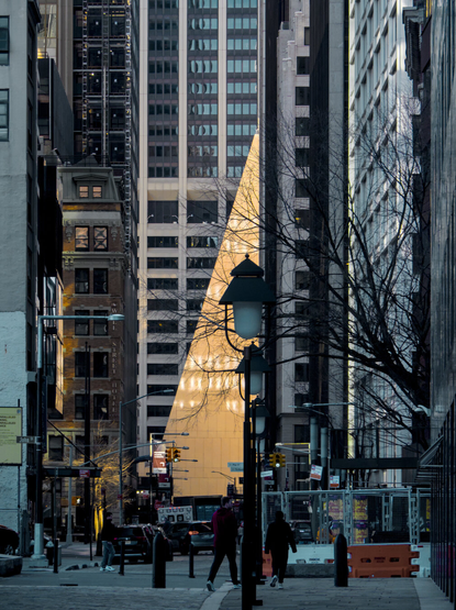 The afternoon sun highlights a triangle shape at the bottom of modern skyscrapers. People were walking in the foreground.