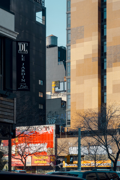 Blocky high-rise buildings with graffiti at the bottom show a slit, where a mid-rise building with a water tower on top peeks out.