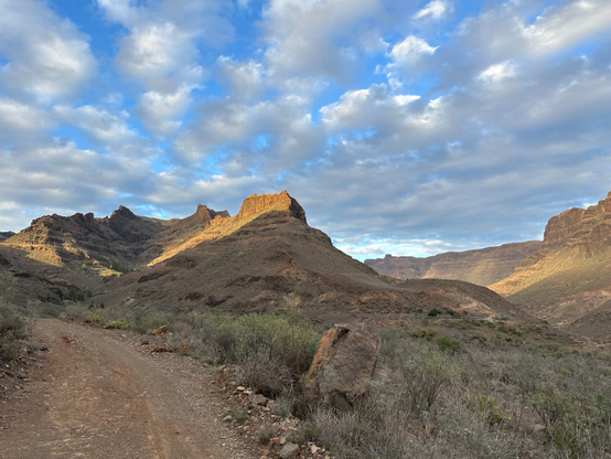 A road through a desert area, with mountain tops lit by the setting sun.