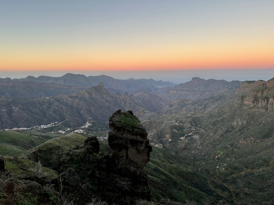 An evening sun highlights the twists and folds of the mountainous terrain. A large rock is stand in the foreground, stout, in contrast to the almost flowing terrain behind it.