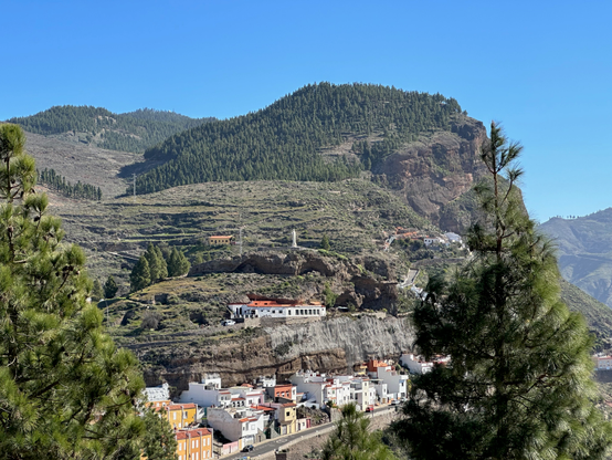 A view of the town of Artenara nestled to the side of a pine-covered mountain.