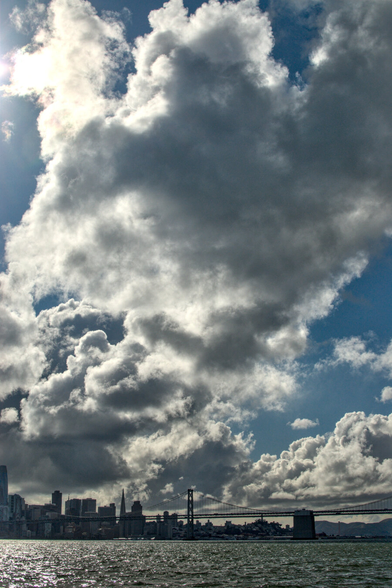 A portrait-orientation photo of dramatic clouds over downtown San Francisco with the Bay Bridge in the foreground