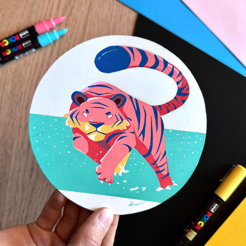 Picture of my hand holding  circle-shaped original illustration painted with poscas featuring a drawing of a leaping tiger.