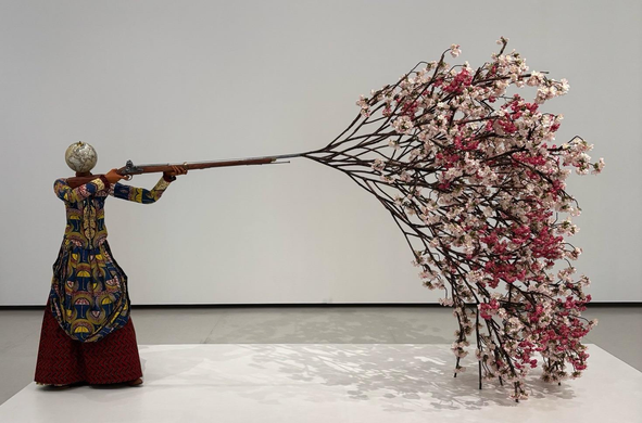 sculpture de grande envergure d'une figure féminine sans tête tirant des fleurs de cerisier avec un fusil 