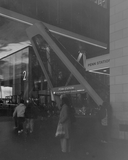 Black and white photo of a glass cone above a subway entrance at Penn Station at night. A woman was standing in the foreground.