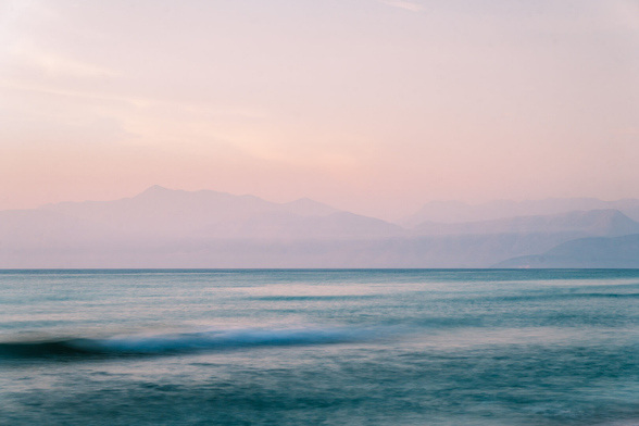 The sea, calm waters on the shore, mountains belonging to Albania visible in the background.