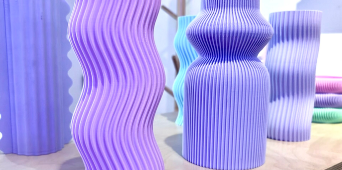 3D printed pastel-coloured vases. Each one is wavy and/or ribbed and/or has fins. They are grouped together on a wood tabletop at a cafe.