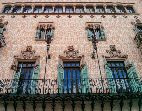 Close-up of the Casa Amatller facade in Barcelona, highlighting two levels of Gothic-style windows with vibrant turquoise shutters and intricate stone carvings.
