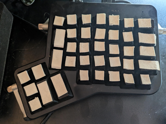 Right side of a well-used Ergodox keyboard on a dusty black desktop. Leather lies atop each keycap, ensuring the typist has a comfortable, tactile typing surface. 