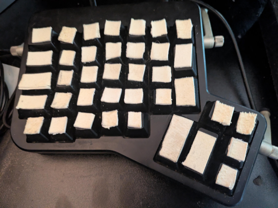 Left side of a well-used Ergodox keyboard on a dusty black desktop. Leather lies atop each keycap, ensuring the typist has a comfortable, tactile typing surface. 