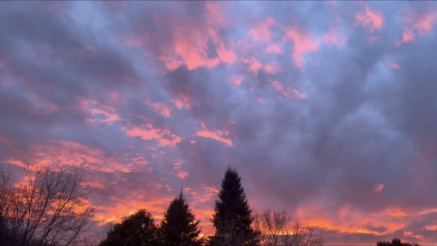 Video showing clouds moving from left to right across the blue sky at sunset, with orange and pink light reflecting off the grey clouds. Trees are visible on the horizon at the bottom.

Vidéo montrant les nuages se déplaçant de gauche à droite dans le ciel bleu au moment du coucher de soleil, la lumière orangée et rosée se reflétant sur les nuages gris. Des arbres sont visibles à l'horizon dans le bas.