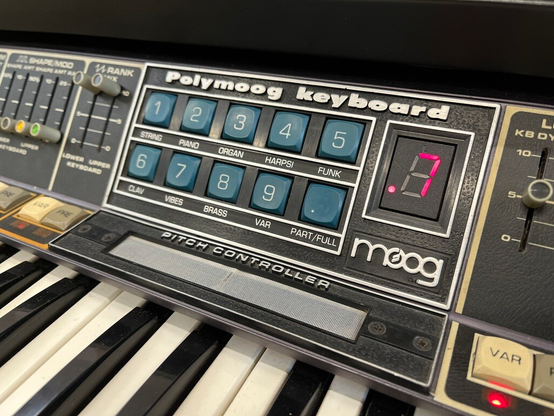 Closeup of a Moog Polymoog preset control section with blue buttons and a 7 digit display. On the bottom is a sliding pitch controller.