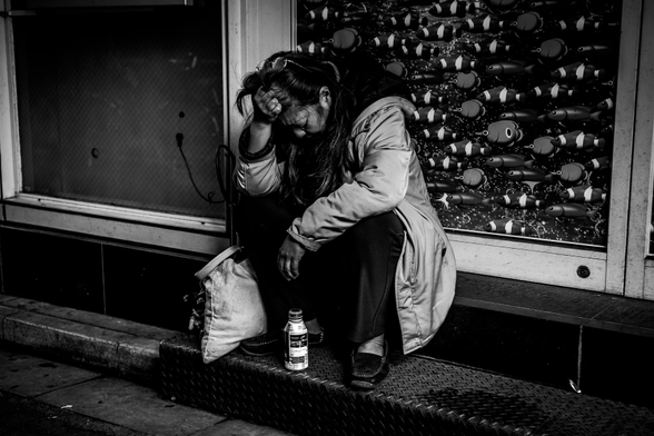 Dona asseguda al carrer amb una ampolla de cafè entre els peus.
