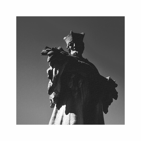 a black and white square image showing a detail of a sculpture of a man with a crown on his head. the sculpture is made out of stone