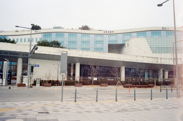 세종시에 있는 국토교통부 건물. 물결치는 듯한 상단부에 작게 '국토교통부'라는 글씨가 보인다. 앞쪽에는 천천히 오른쪽으로 내려오는 건물과, 입구 게이트, 담장 등이 보인다. 한산하고 차량이 없다.