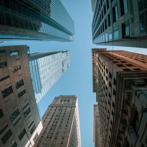 Wide-angle photo looking straight up between tall downtown skyscrapers on a clear blue day.