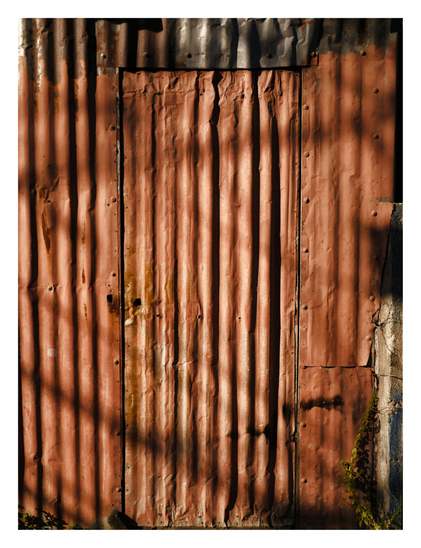 A weathered, rusty corrugated metal wall with a makeshift door cut into the center. The reddish-brown metal is dented and held together with rivets, while strong, distinct shadows fall vertically across its surface. - Google Gemini 3.1 Pro Preview
