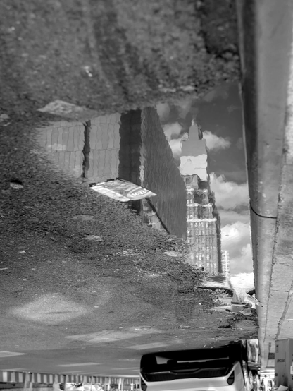 A puddle lined with trash reflects the old high-rise buildings. The photo was flipped to make the reflections of the buildings look upright.