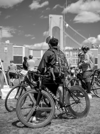 A track bike with aero wheels leans on a man who was walking to other people, with a tower of the Verrazano Bridge in the background