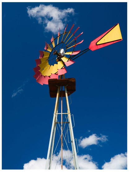 Blick von unten auf ein Western-Windrad: Flügel und Fahne in den spanischen Farben Gelb und Rot bemalt, dahinter blauer Himmel mit weissen Wolken.