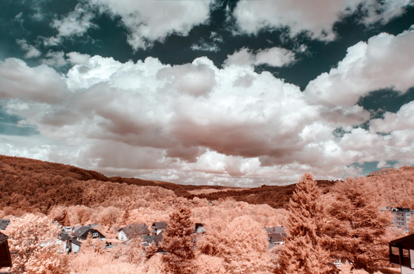 A landscape shot of a valley with brown-orage foliage, white clouds obstructing a dark teal sky