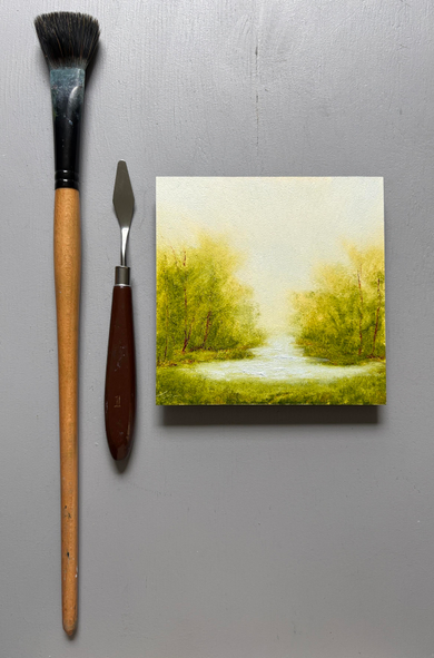 Original landscape oil painting study by Tisha Mark, shown with a paintbrush and palette knife for scale. Trees with soft green leaves and soft green grasses surround a small pond. The sky is a soft light gray with a warm undertone.  