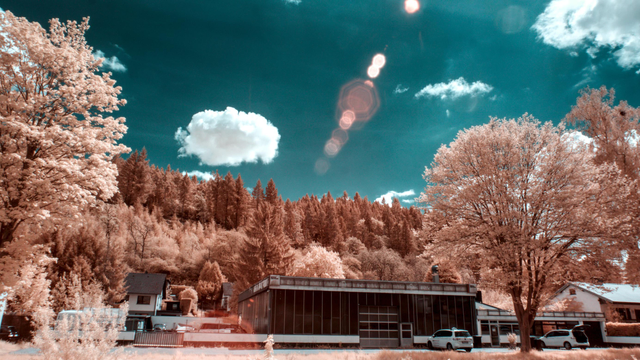 A dark car garage building in front of a hill top, with trees and a red solar flare in the sky
