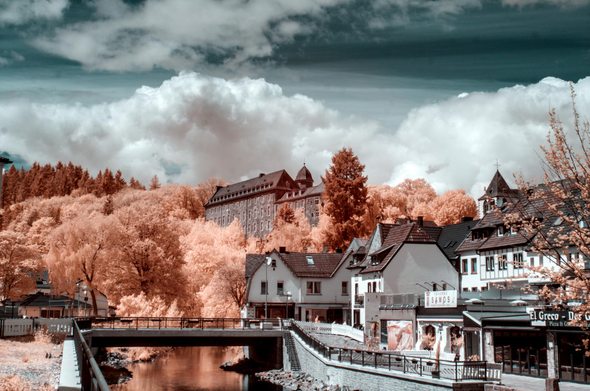An old town with a river flowing through it, a castle on a hill behind it and clouds on top