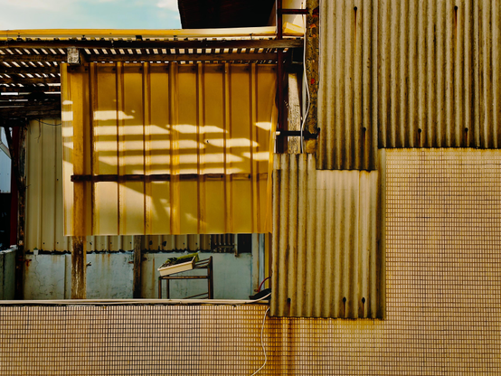 Close-up of a weathered building with yellow, corrugated, and tiled metal panels, creating an abstract pattern.