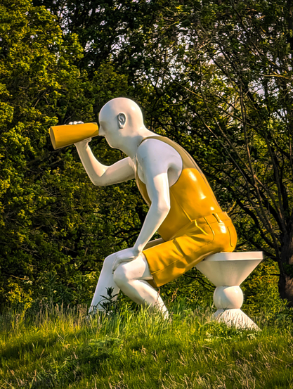 A large, stylized outdoor sculpture of a human figure, wearing bright yellow clothing consisting of a sleeveless tank top and matching shorts.

The figure is seated on a white pedestal-style stool. It is leaning forward slightly, with its left hand resting on its knee. With its right hand, it holds bright yellow binoculars.

It's part of a larger installation with several oversized godwits to symbolize the bird reserve in Eemnes.