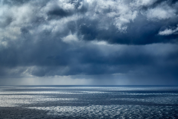 seascape with sea taking the bottom third of the photo and stormy clouds at the top. The light shines through the gaps making light patches on the sea surface