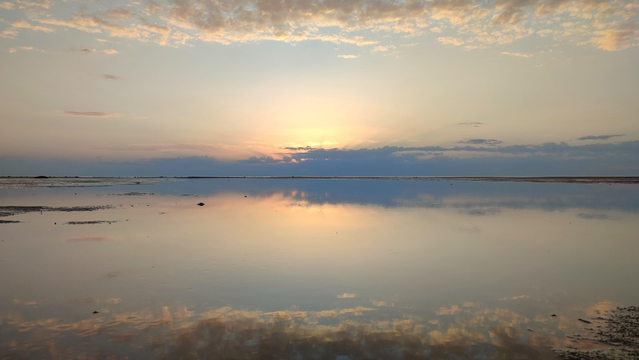 Farbfoto im Querformat. Sonnenuntergang über der sehr flachen und spiegelglatten Ostsee. Wolken und Sonne spiegeln sich im Wasser.