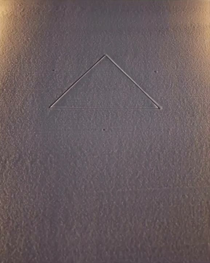 une main trace des figures géométriques sur le sable avec un râteau à quatre dents