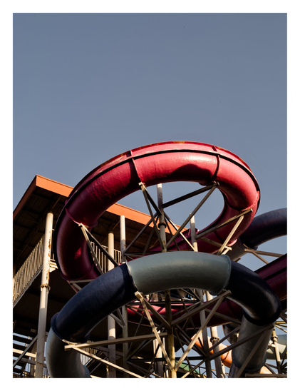 A complex structure of intertwined, tubular water slides in faded red and blue, supported by a metal framework against a clear blue sky. - Google Gemini 3.1 Pro Preview