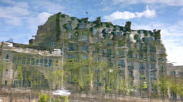 Photo du reflet d'un bâtiment style parisien dans l'eau du canal Saint-Martin. Quelques ondulations déforment l'image.