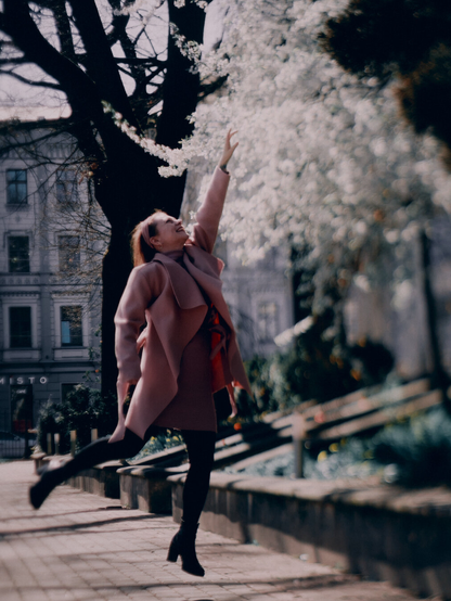 Photo of a young woman in pink clothes jumping up to touch blooming tree in a city park shot with tilt lens.