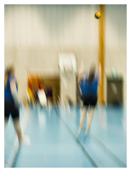 En stående bild på en volleybollmatch tagen med lång slutartid som följer bollen. Alla spelare, linjer och golv är suddiga. Endast bollen högt uppe i luften är skarp.